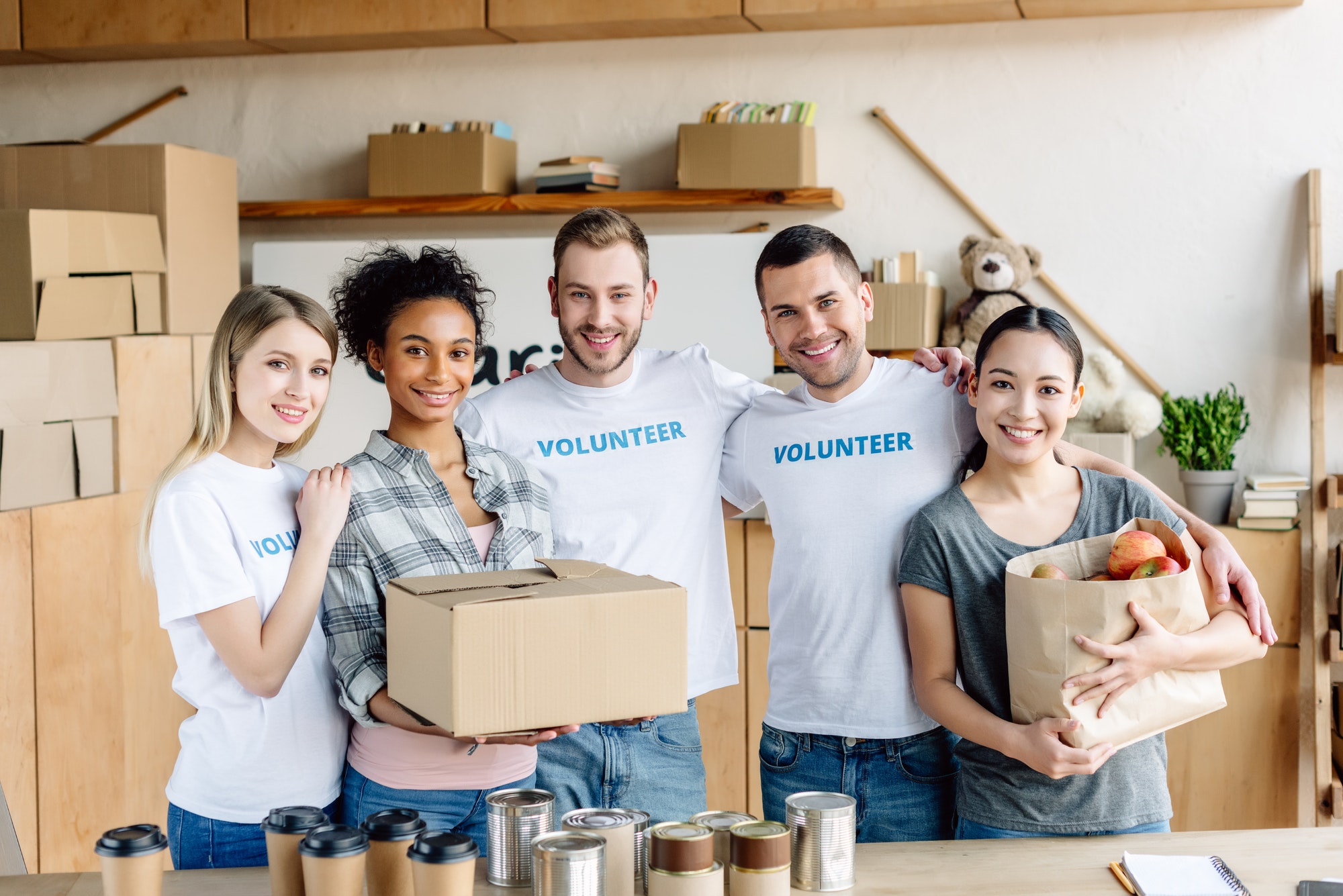 happy-multicultural-women-holding-cardboard-box-and-paper-bag-with-apples-while-standing-near.jpg