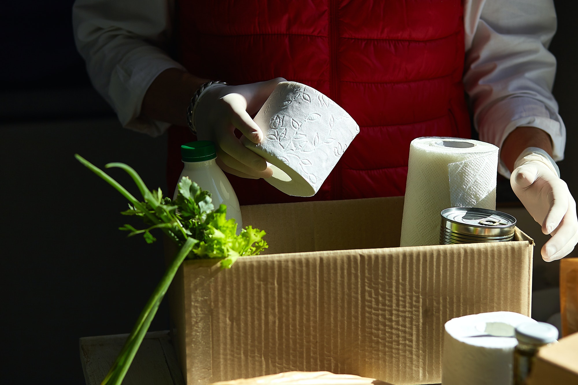 Volunteer in the protective medical mask and gloves putting food In donation box.