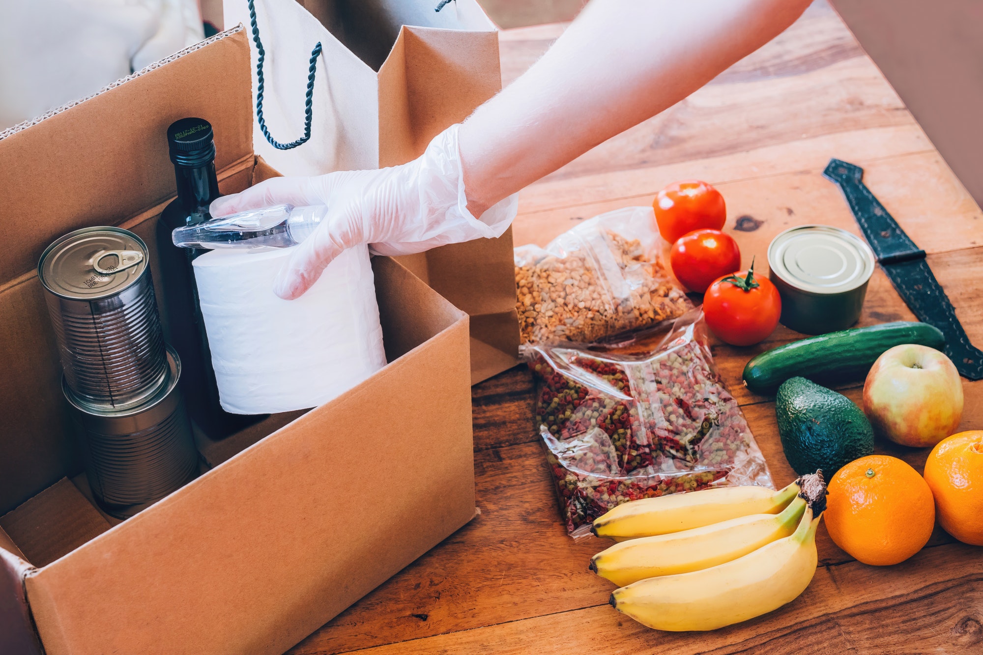 Woman's hand puts food, toilet paper, and hand sanitizer to the carton box for donation.